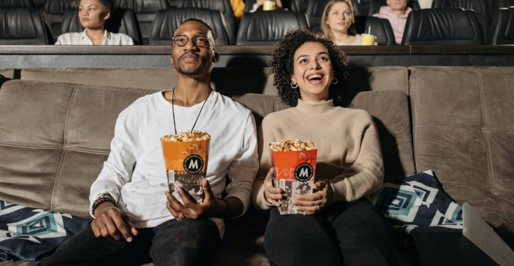 two people at the movies watching slapstick comedy with popcorn